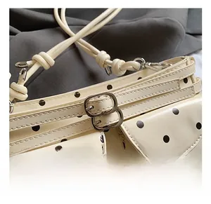 Close-up of cream polka dot shoulder bag with silver metal buckles and knot strap