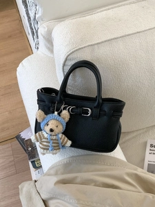 Elegante schwarze Handtasche mit Teddybär-Anhänger auf einem minimalistischen Sofa
