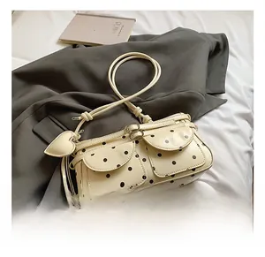 Close-up of cream polka dot shoulder bag featuring dual front pockets and a heart charm