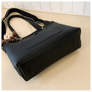 Détail du cabas noir grainé avec bandoulière large et breloque en peluche pour femme