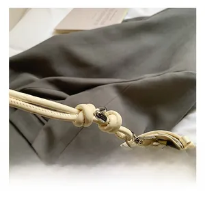 Detail shot of beige leather shoulder bag featuring metal hook and knotted strap design