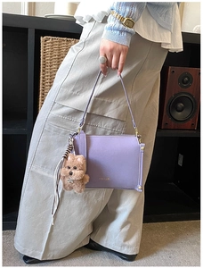 Close-up of purple leather shoulder bag with golden logo and cute plush bear charm