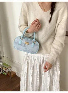 Détail du sac Boston bleu clair texturé avec logo doré et poignée en cuir élégante