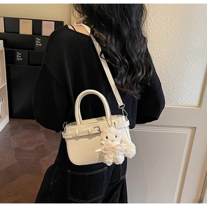 Dettaglio di una borsa in pelle bianca con un ciondolo a forma di gatto in peluche sulla tracolla