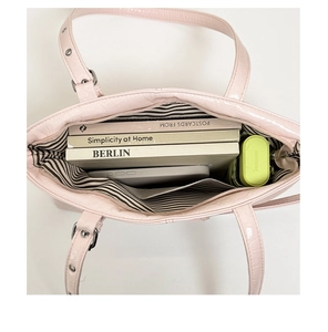 Dettaglio della borsa tote in pelle verniciata rosa con fodera a righe e ampia capienza