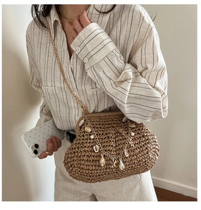 Detail of woven straw beach bag with shells and pearls showing crossbody fit on model