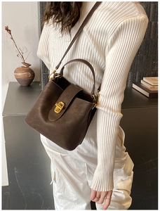 Detailed view of brown suede bucket bag with gold twist lock on knit sweater background