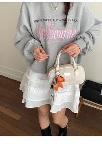 Détail du sac Boston en tissu blanc cassé avec un charm de cheval en cuir orange vif