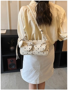 Close-up of cream shoulder bag with black polka dots featuring front pockets and tassels