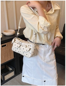 Detail of white rectangular shoulder bag with black polka dots and dual front flap pockets