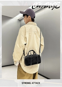 Detail view of black leather Boston bag with adjustable shoulder strap on a male model