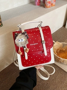 Red polka dot mini backpack with white trim and a cute plush monster charm