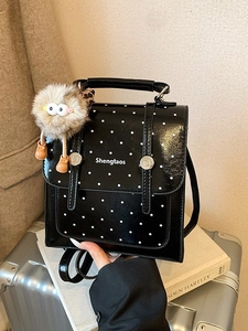 Black polka dot mini backpack with plush monster charm on silver suitcase display