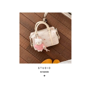 Detail der cremeweißen Handtasche mit Print, Doppelgriffen und süßem Teddybär-Anhänger