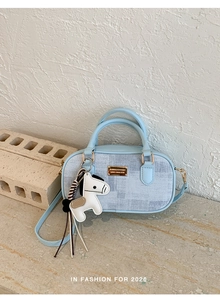 Détail du sac Boston bleu clair avec texture tissée, plaque en métal et breloque