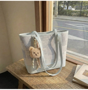 Détail du sac seau en cuir bleu avec motif géométrique et pendentif ours en peluche