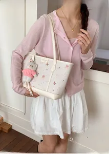 Close-up of white tote bag with purple bear print and plush bear charm on white dress