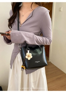 Dettaglio borsa sottobraccio in pelle nera con ciondolo floreale e scritte moda