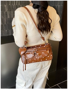 Close-up of brown polka dot shoulder bag featuring dual buckle pockets and heart charm