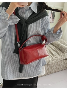 Close-up of a red vintage crossbody handbag with glossy finish on a grey plaid shirt