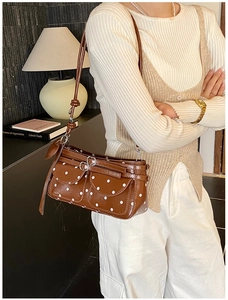 Detailed side view of a brown polka dot shoulder bag with stylish metal buckle pockets