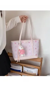 Detail of pink tote bag with bow prints and cute teddy bear charm on wood background