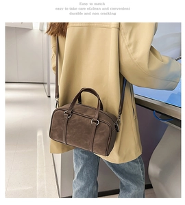 Detail of a dark brown suede Boston bag with double handles and a detachable shoulder strap