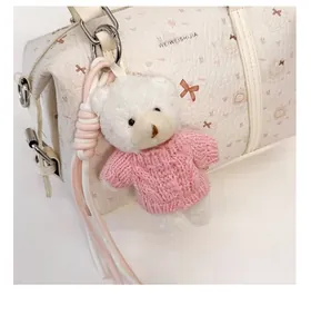 Detail eines weißen Plüschbär-Anhängers mit rosa Strickpullover an einer Handtasche