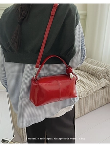 Close-up of red patent leather cylindrical crossbody bag worn by a model in casual style