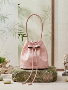 Pink bucket bag with floral jacquard texture and bow detail on a mossy stone base