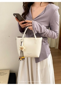 Dettaglio della borsa in pelle color crema con ciondolo floreale in legno e design a trapezio