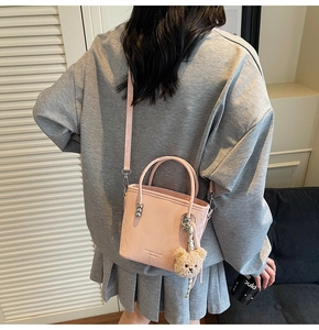 Pink bucket bag with metal ring handle and plush bear charm shown on a model