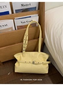 Close-up of pale yellow glossy tote featuring decorative belt buckle and eyelet straps