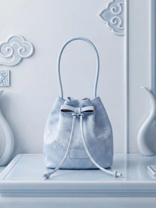 Elegant light blue bucket bag with floral embroidery and bow detail in a minimalist scene