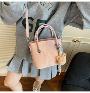 Pink bucket bag with crinkled texture, plush bear charm, and adjustable crossbody strap