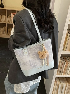 Sac seau patchwork bleu avec imprimé journal et breloque ours porté à l'épaule