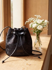 Elegant black bucket bag with embossed floral texture and bow drawstring on a sunny window