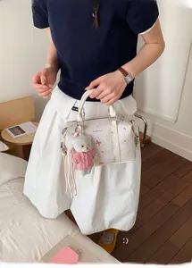 Detailaufnahme der weißen bedruckten Schultertasche mit rosa Schleifen und Bärenanhänger