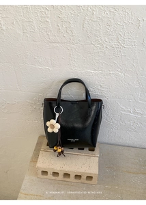 Dettaglio di borsa tote vintage nera in ecopelle con ciondolo floreale su base
