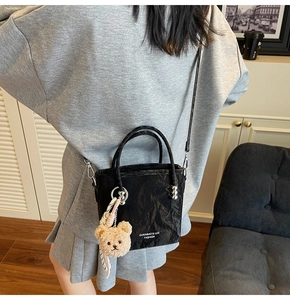 Model back view of a black pleated bucket bag with cute bear charm and shoulder strap