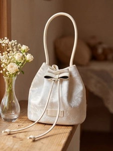 White bucket bag with floral embroidery and bow tie shown in a soft indoor setting