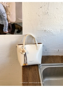 Dettaglio borsa tote in pelle crema con ciondolo a nappa floreale e stampa di testo