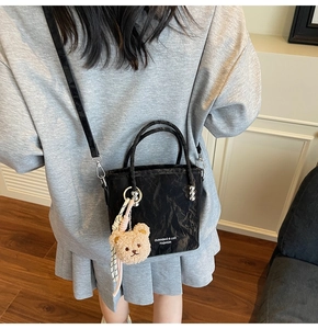 Detail of black textured bucket bag with plush bear charm and removable shoulder strap