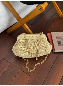 Close-up of woven straw clutch bag with gold chain featuring seashell and pearl charms