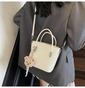 Detailed view of cream leather bucket bag with plush bear charm and metallic bead detail