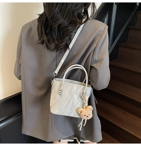 Detail of silver pleated bucket bag with plush charm on a wooden staircase background