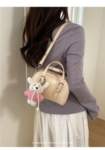 Detail of minimalist beige Boston bag with knit bear pendant and detachable shoulder strap
