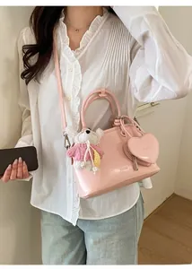 Detailed shot of pink glossy shell bag with heart charm and white plush bear accessory