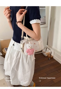 Detail der cremefarbenen Zylindertasche mit Mini-Prints und Plüschbär-Anhänger am Model