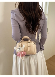 Detail of beige retro handbag featuring a cute knit rabbit charm and buckle straps